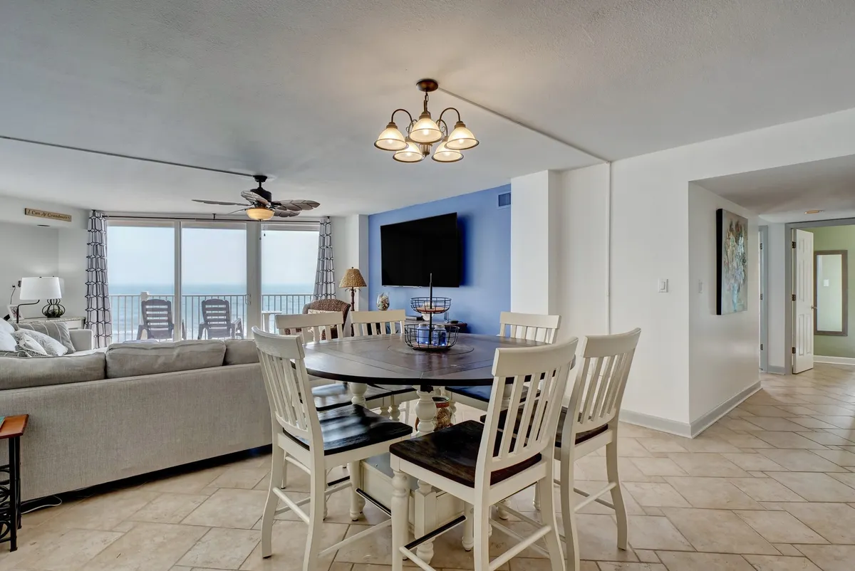 An elegant dining area with a table set for meals, positioned in front of large windows that frame an unobstructed ocean view. The adjacent cozy seating area and decorative lighting create a comfortable, stylish atmosphere.
