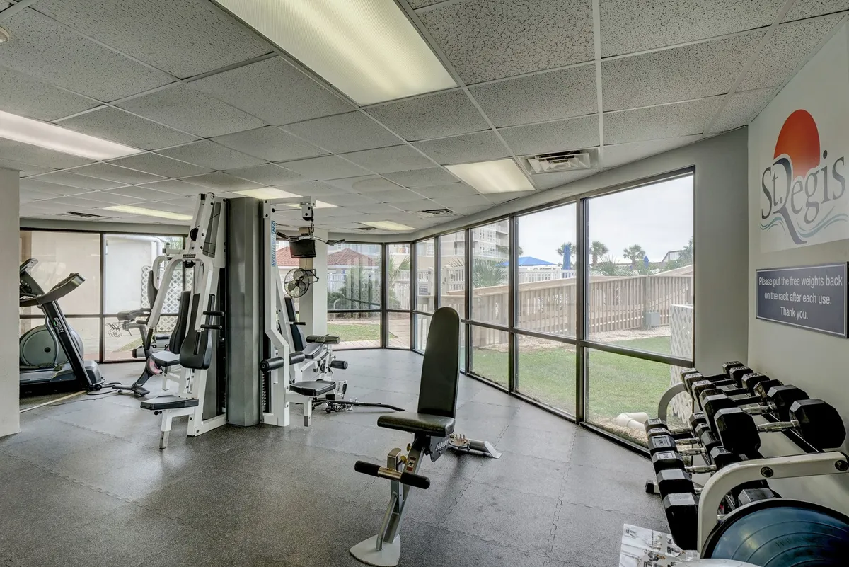 A modern fitness center filled with exercise machines and free weights, flooded with natural light from large windows. The space feels energetic and motivating, perfect for a quick workout between meetings or to unwind after a productive day.