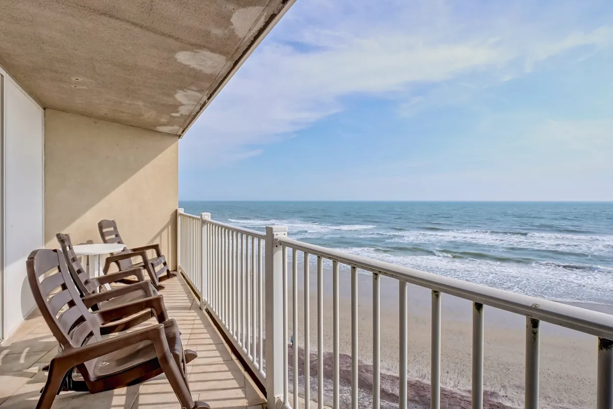 This image showcases balcony chairs positioned for relaxation, overlooking a sweeping ocean view with the beach and sky in the distance. The setting suggests a serene spot for morning coffee or evening unwinding, directly connecting guests to the coastal environment.