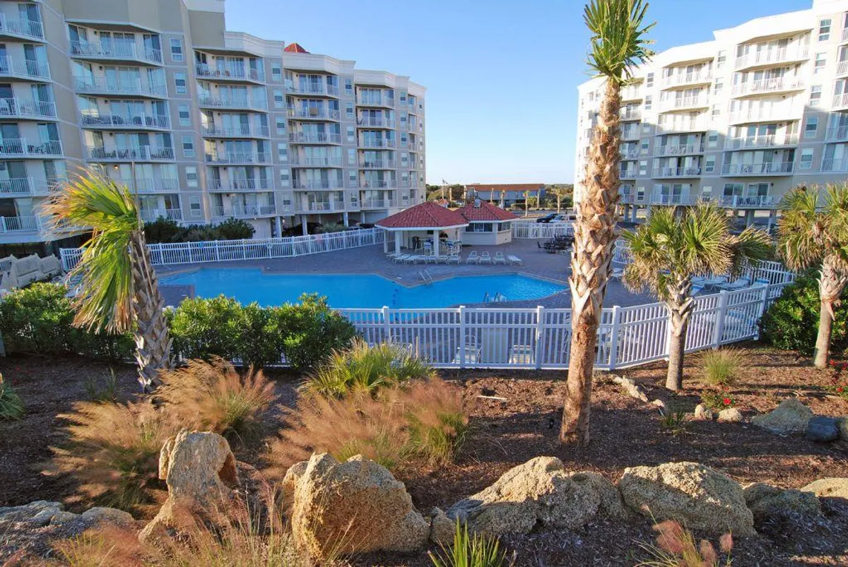 A vibrant outdoor swimming pool encircled by palm trees and resort buildings, with poolside cabanas providing a leisurely atmosphere perfect for group gatherings, sunbathing, or socializing before or after on-site activities.