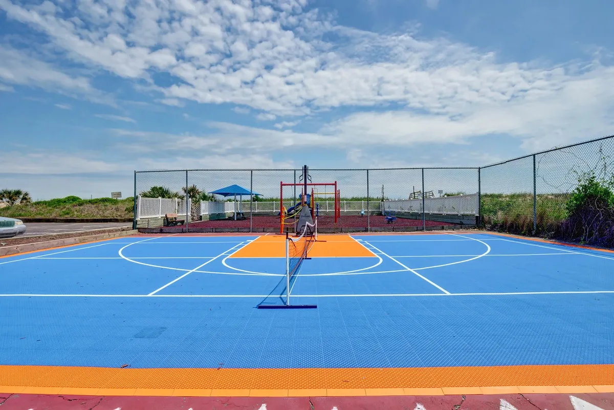An energetic exterior shows a brightly colored basketball and pickleball court, with a net and playground equipment visible in the background. The space is set up for friendly competitions and active afternoons for both teens and adults.