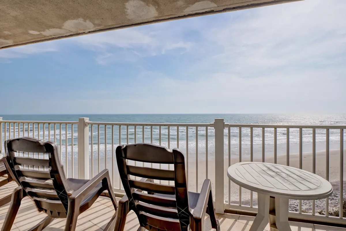 The image captures a tranquil balcony scene overlooking an expansive ocean view. Two comfortable patio chairs and a round table invite guests to relax, sip coffee or cocktails, and soak in the fresh sea breeze. The setting hints at peaceful mornings watching the sunrise, cozy evenings spent stargazing, and memorable intimate gatherings with loved ones.
