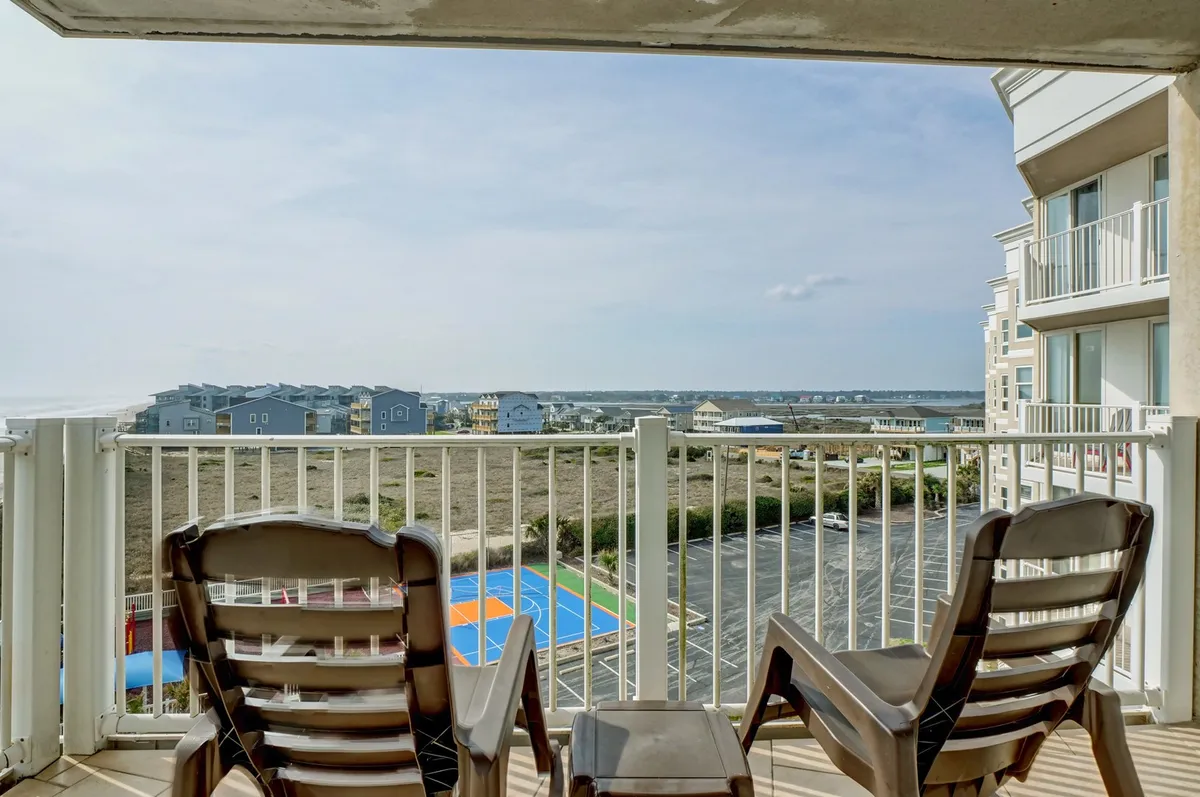 A serene balcony setup with comfortable chairs and a clear view of the ocean and a colorful court below. The space is perfect for reading, relaxing, or enjoying a sunset. The beach is visible just beyond the balcony, reinforcing direct access to nature and leisure.