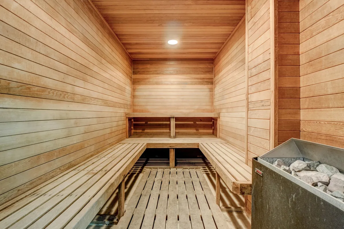 A tranquil sauna interior lined with warm wood paneling, featuring a stone heater and wooden benches for guests to unwind and rejuvenate.